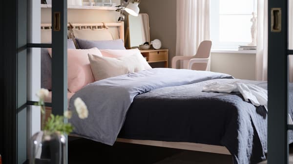 A bedroom with a BJÖRKSNÄS birch bed, dark-blue KOPPARBLAD bed linen, a NORDKISA dressing table and an ODGER swivel chair.