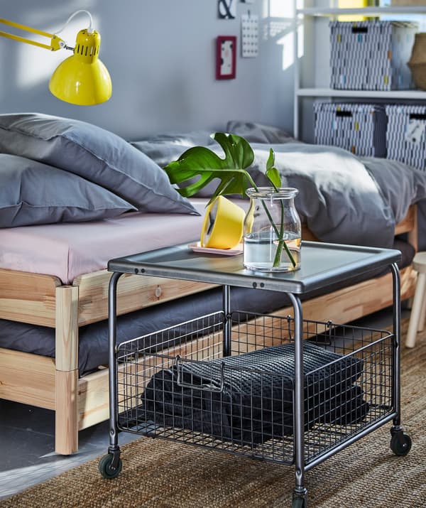 A bedroom with a coffee table with an open wire basket underneath used for storing bed linen.