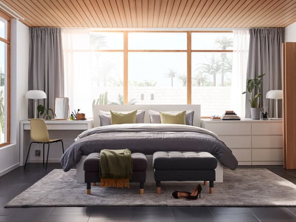 A bedroom with a dressing table, a bed frame and a chest of drawers from the MALM series and a large grey rug on the floor.