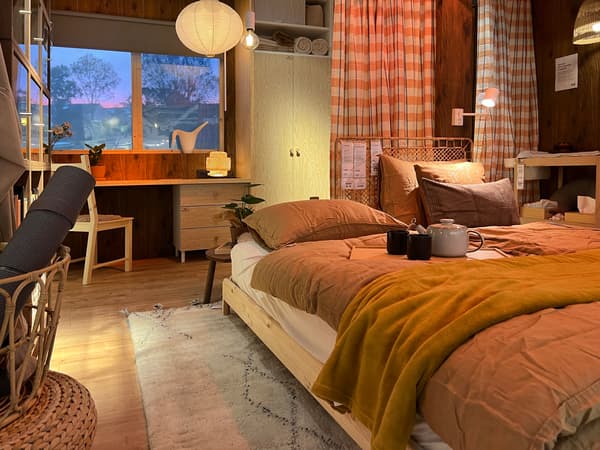 A bedroom with a natural look with a wooden floor, wooden bed, checkered curtains and a wooden chair with desk.