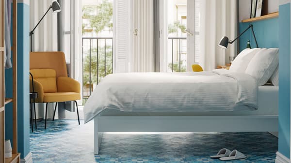 A bedroom with a white bed with white bedlinen, blue walls and floors and a yellow armchair.