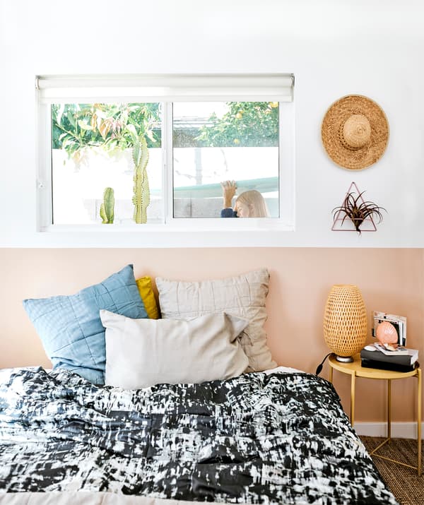 A bedroom with black and white bedding, books and lamps on a bedside table, and Chloé walking past the window behind the bed.