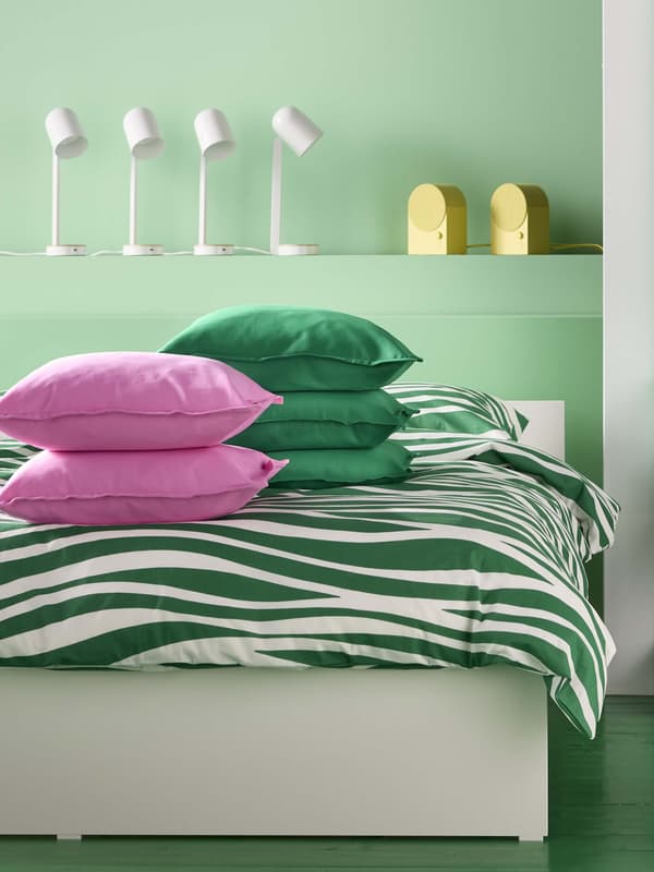 A bedroom with green and white wavy striped bedding and pink and green pillows on top.