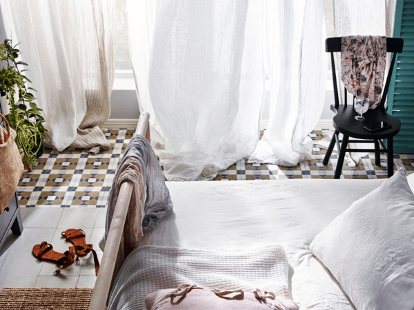 A bedroom with large windows behind full curtains that appear to be swaying in the breeze.