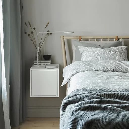 A bedroom with layers of bedding in neutral colours and a white wall-mounted bedside unit.