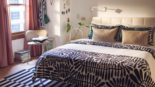 A bedroom with pink curtains and the MAJSMOTT black and white comforter set with a large leaf pattern on it.