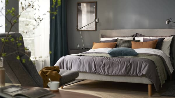 A bedroom with tan, blue and gray bedding and an upholstered bed frame.