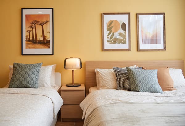 A bedroom with two bed of different sizes with a bedside drawer separating them.