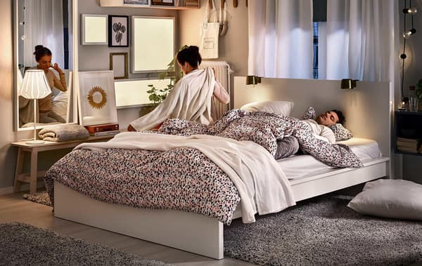 A bedroom with two people, a double bed and various lighting.