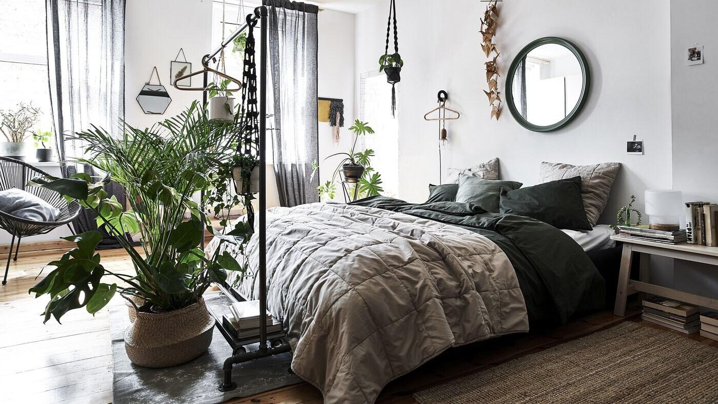A bedroom with white walls, natural-coloured bedding and plants in wicker baskets.
