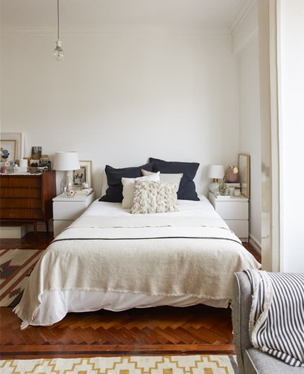 A bedroom with wooden floor, white walls and layered bedding.