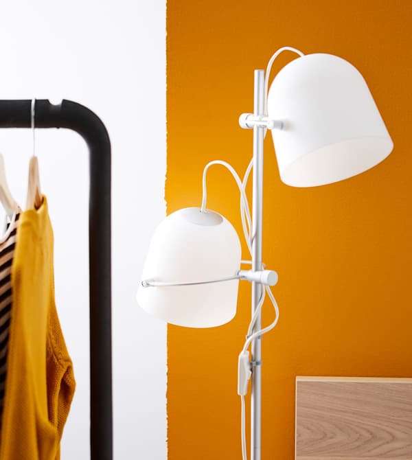 A bedside floor lamp with two plastic shades stands next to an orange wall.