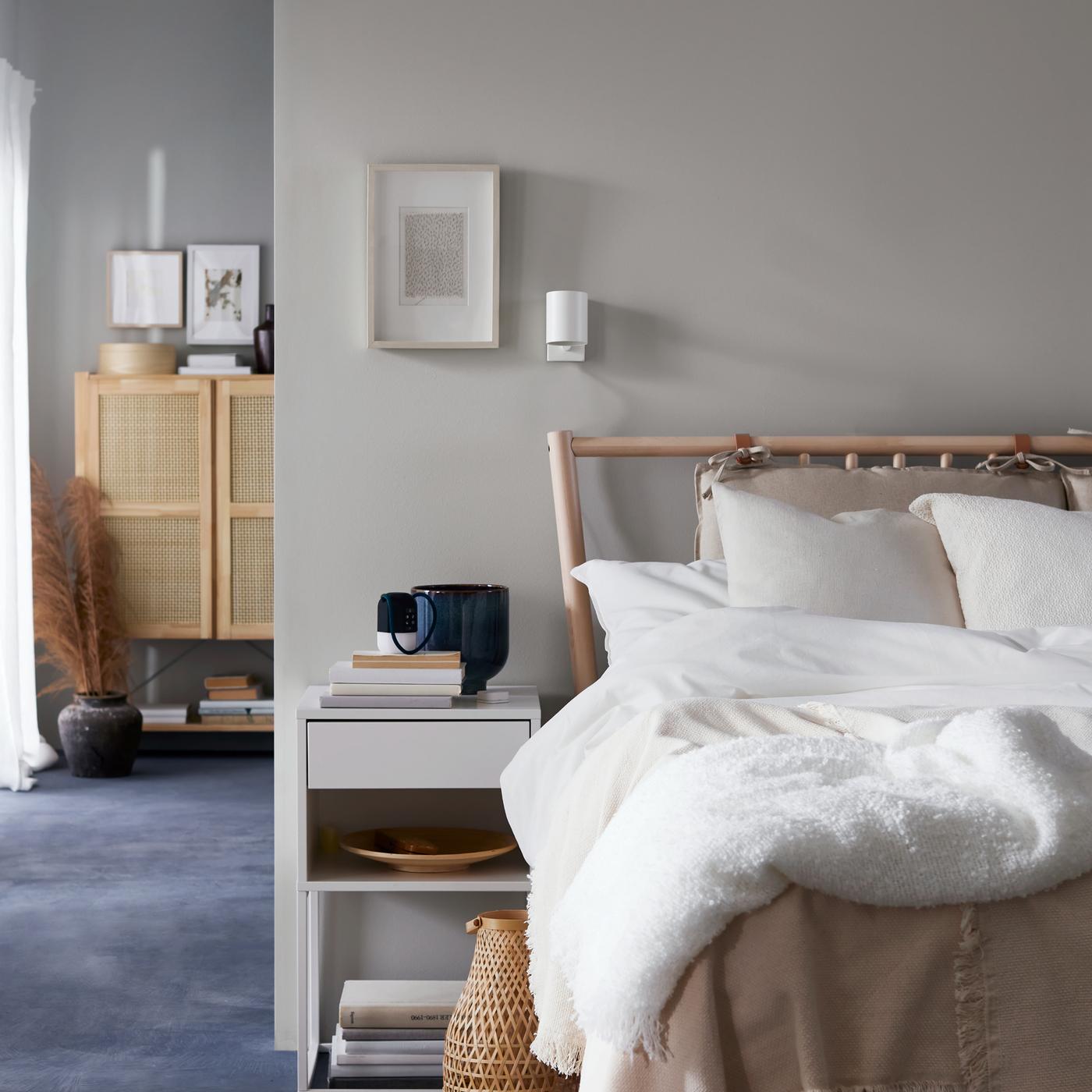 A bedside table stands under a picture in a white frame on a wall and beside a birch BJÖRKSNÄS bed with white bed linen.