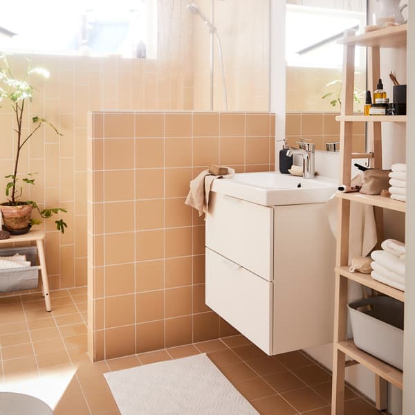 A beige coloured bathroom room, with a white sink unit and an IKEA VILTO shelving unit in birch.