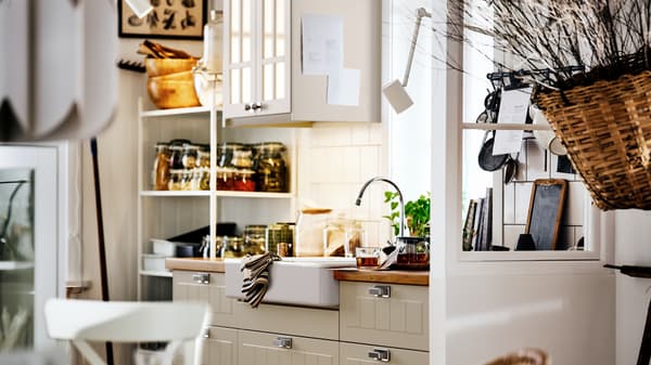 A beige country-style kitchen with STENSUND fronts on METOD cabinets, a white sink and shelving with jars and utensils.