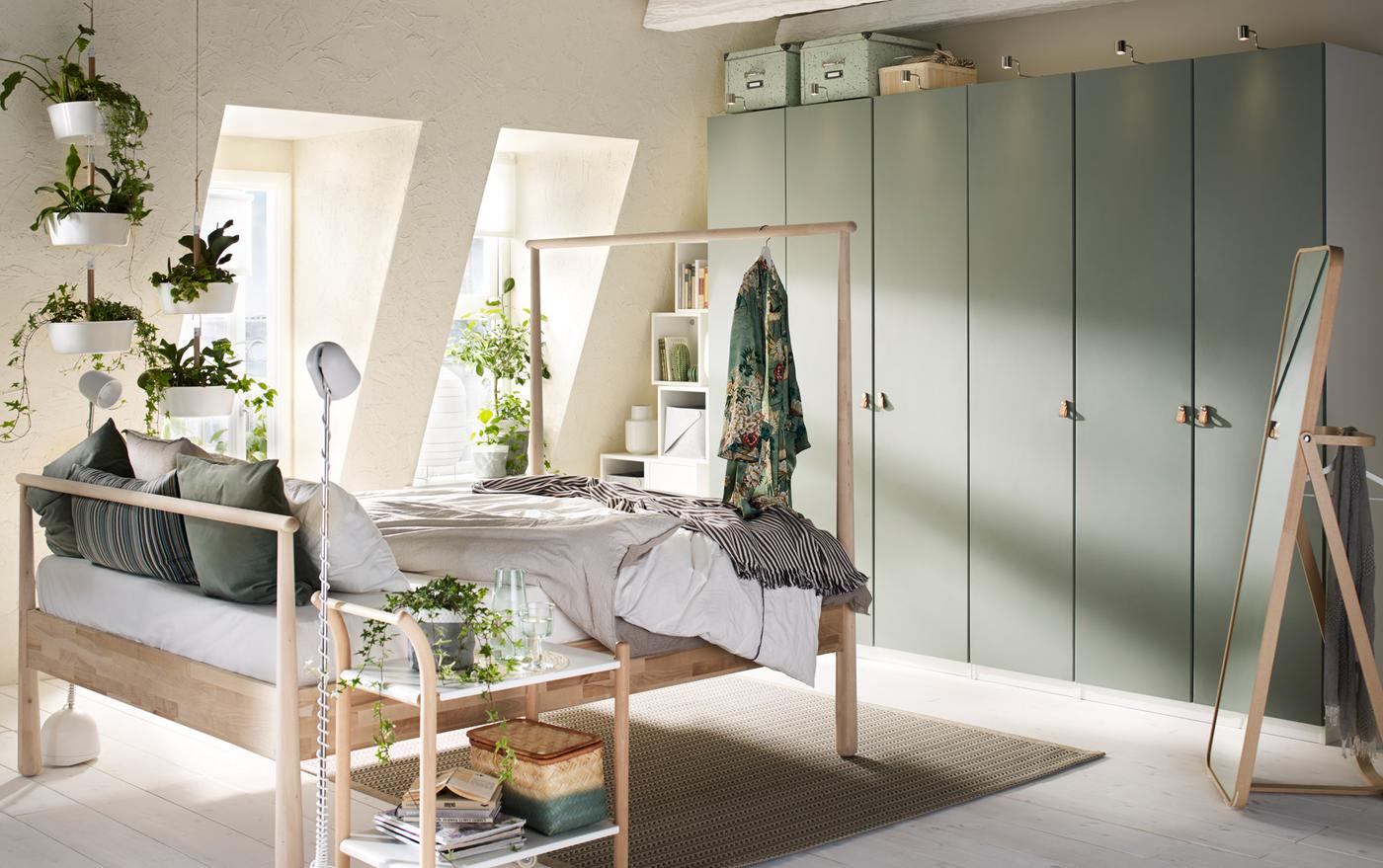 A beige, green and grey bedroom with grey-green wardrobes across the back wall and a wooden bed in the centre.