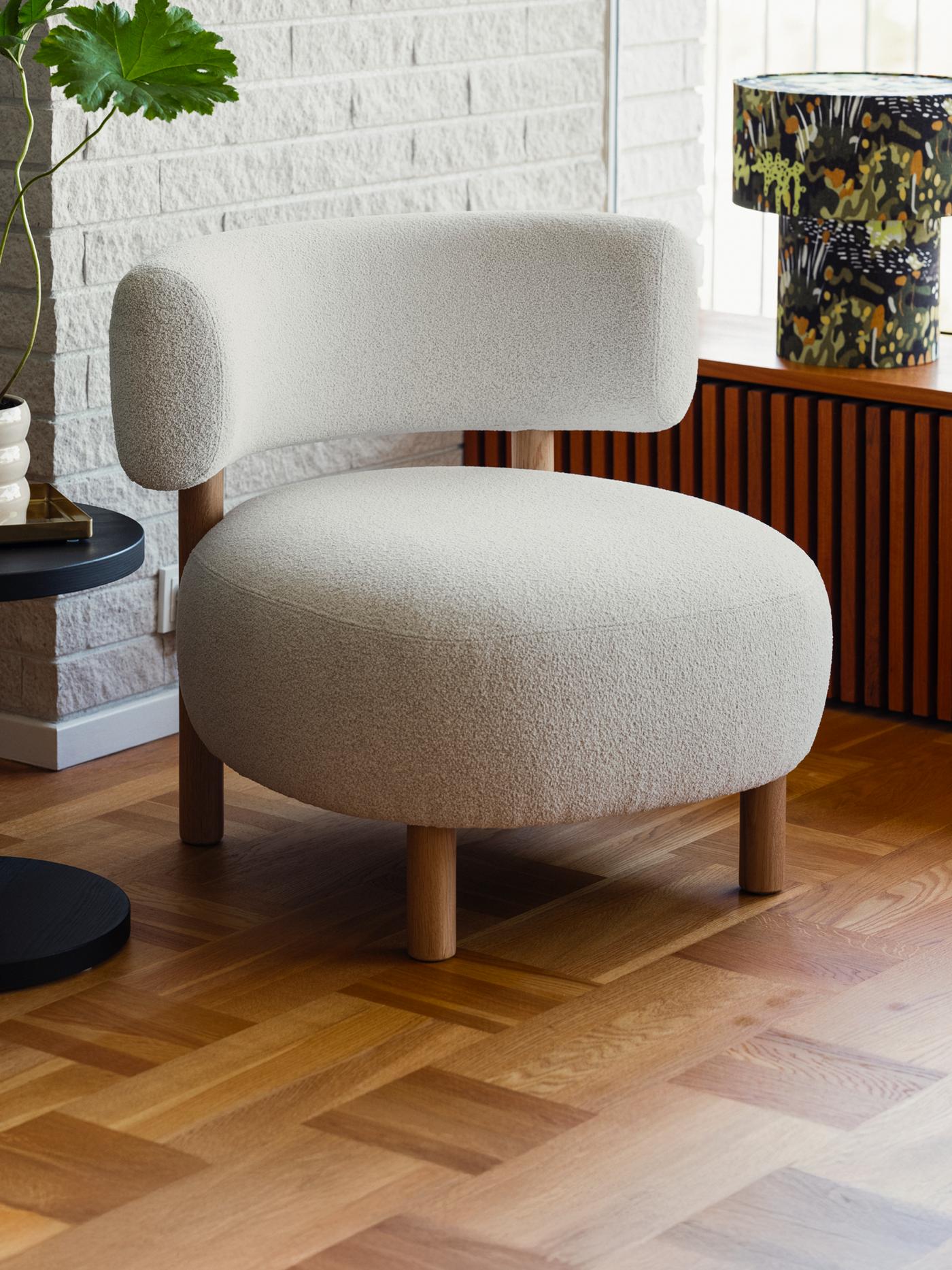 A beige STOCKHOLM 2025 armchair on parquet flooring by a white brick wall, a black pine veneer side table next to it.
