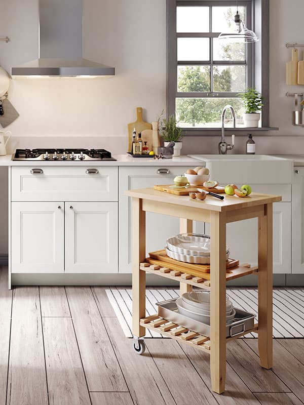 A BEKVÄM kitchen cart on castors is standing by a stove, apples are being peeled and sliced on its top surface.