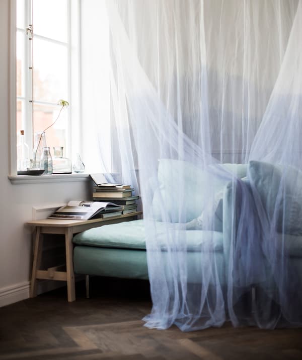 A bench and an IKEA SÖDERHAMN corner section are placed in front of a window and draped with a canopy to make a cosy reading space.