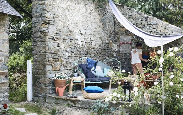 A bench, chairs and side tables with colourful cushions in a walled garden area.