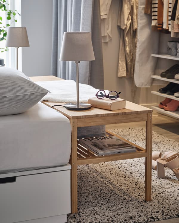 A bench in bamboo stands by a bed and is used as a bedside table. Table lamps, glasses and a book are on its top surface.