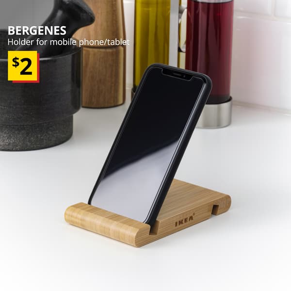 A BERGENES bamboo holder for mobile phone/tablet placed on the desk. White text on top left of the image reads: BERGENES, Holder for mobile phone/tablet. Price: $2