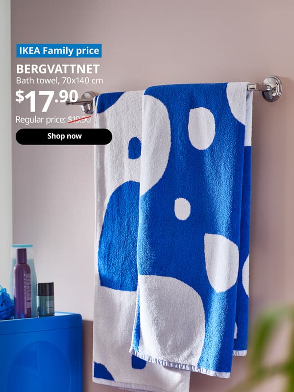 A BERGVATTNET bath towel with reversed blue/white drop pattern on each side hung on a towel rail in the bathroom. White text of blue tag that reads "IKEA Family price". White text over image that reads "BERGVATTNET, Bath towel, 70x140 cm. Price $17.90. Regular price: $19.90 with red line slashed across.