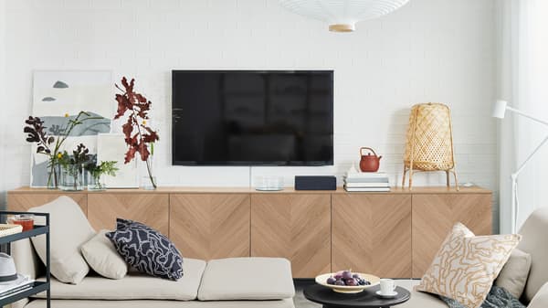 A BESTÅ storage combination with HEDEVIKEN doors in oak veneer beneath a TV screen mounted on a white-brick living room wall.