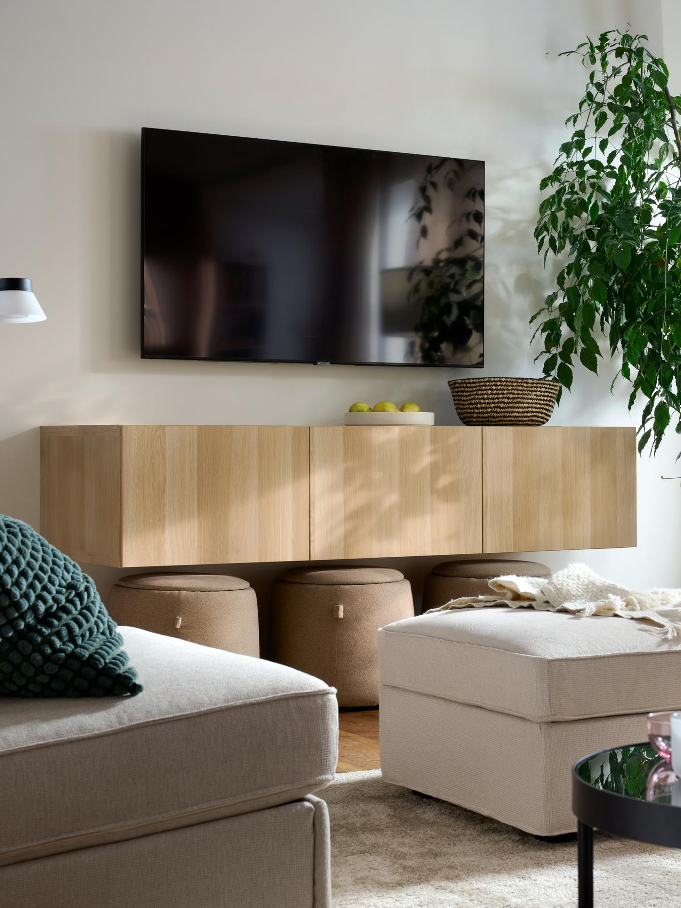 A BESTÅ TV bench with doors in white stained oak effect is mounted below a TV with tresund light beige footstool placed below in a living room setting.