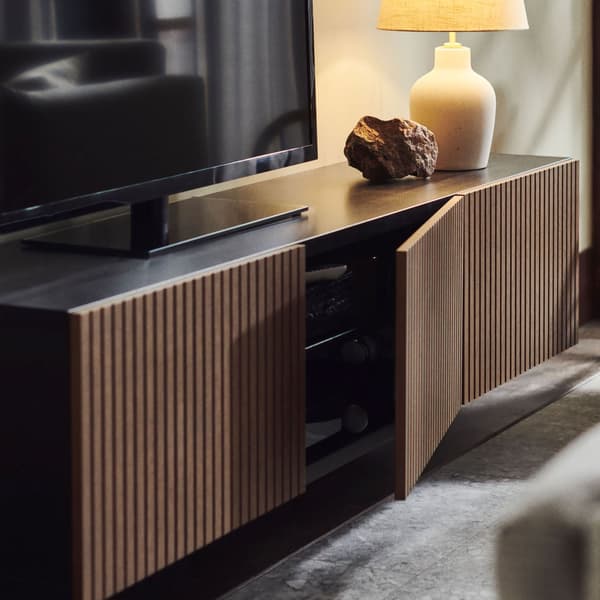 A BESTA TV cabinet with brown doors with a TV and a table lamp on top.