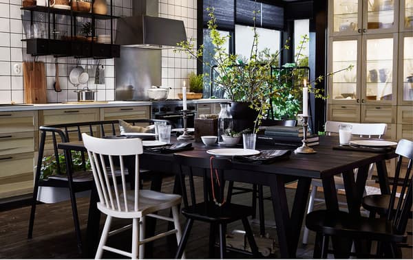A big dark wood dining table with lots of chairs in the middle of a modern swedish kitchen.