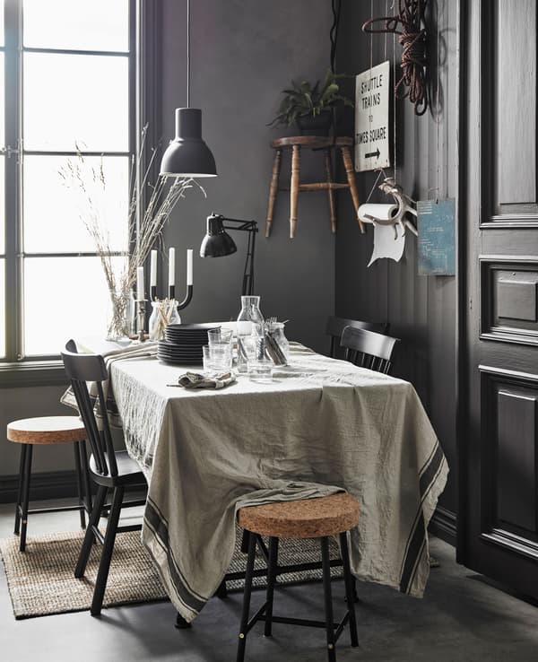 A big dining table partly covered in work papers with a linen table cloth and dishes covering the rest of the table