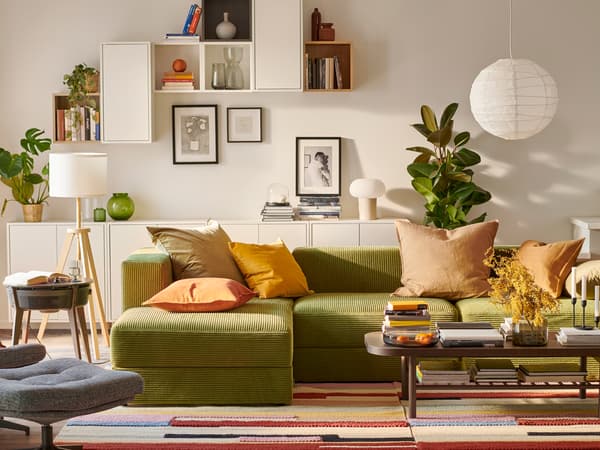 A big green JÄTTEBO modular sofa sits in a light bright living room. The wall behind has eclectic EKET shelving and artwork.