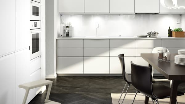 A big white kitchen with matt white kitchen doors and drawer fronts, a white worktop and a dark brown table with two chairs.