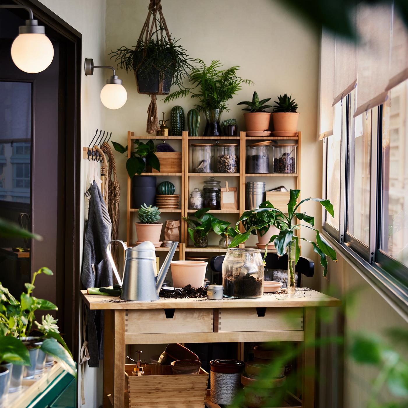 A birch FÖRHÖJA kitchen trolley, bamboo shelving units and a green cabinet with plants and gardening items all around.
