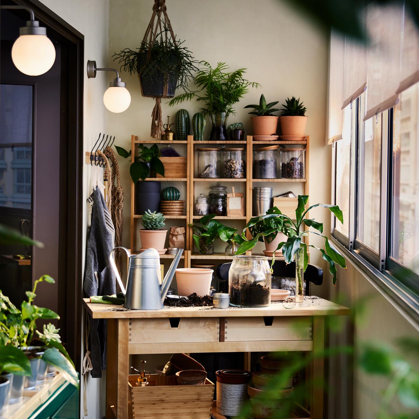 A birch FÖRHÖJA kitchen trolley, bamboo shelving units and a green cabinet with plants and gardening items all around.