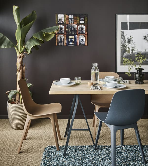 A birch KARLBY worktop with trestles legs and ODGER chairs create a dining area in a living room with dark brown walls.