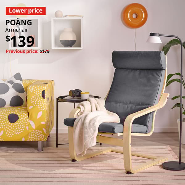 A birch veneer/Skiftebo dark grey POÄNG armchair in a living room setting. An red "Lower price" label is on the top left of the image with black text that reads: POÄNG, Armchair, $139. Previous price with red slash $179.