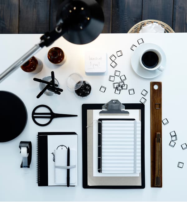 A bird’s-eye view of a home office desk with work supplies like paperclips, pens, and coffee.