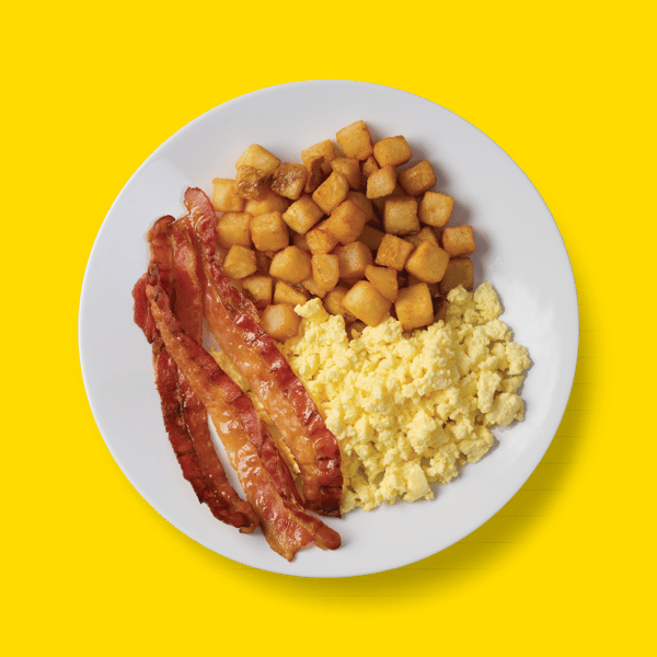 A birds eye view of a plate with eggs, bacon and hash browns against a yellow background.