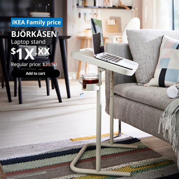 A BJÖRKÅSEN laptop stand with a laptop placed in a living room setting. On the top left corner, a blue tag with white text that reads 