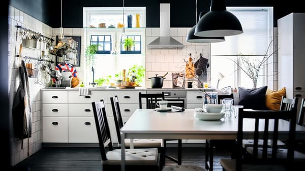 A black-and-white kitchen with white METOD cabinets with MAXIMERA interiors and a dining area with two white MELLTORP tables.