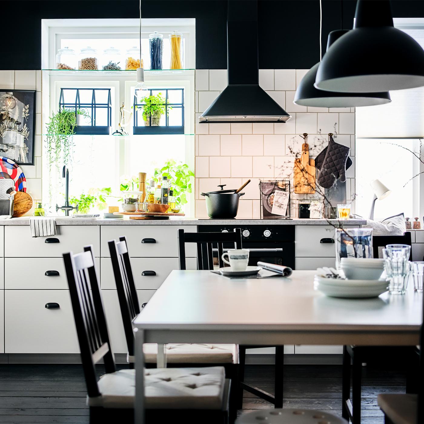 A black-and-white kitchen with white METOD cabinets with MAXIMERA and a dining area centred around two white MELLTORP tables.