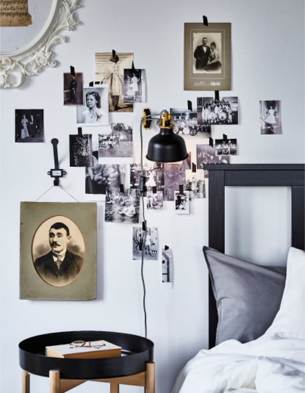 A black and white photo wall created around a bedframe and lamp.