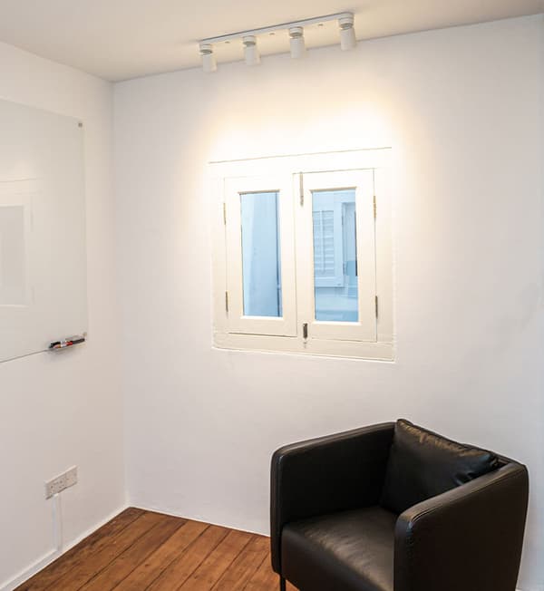 A black armchair placed against the corner of a white room.