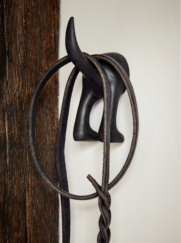 A black BÄSTIS hook in the shape of a cat's behind, with a leash hanging from the curved tail.