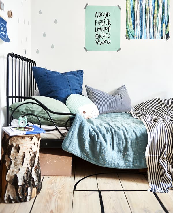 A black bed frame with green and blue bedding and posters on the wall.