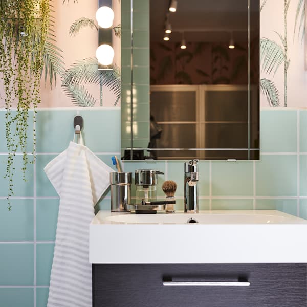 A black-brown wash stand, a white wash basin, a mirror and lighting by it, and a striped towel in a pink/green bathroom.