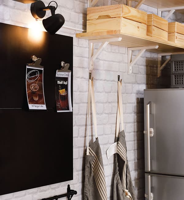 A black bulletin board as well as aprons hung on hooks against a white bricked wall. 