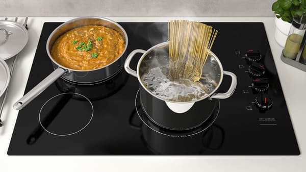 A black cooktop with pasta cooking in a stainless steel pot.
